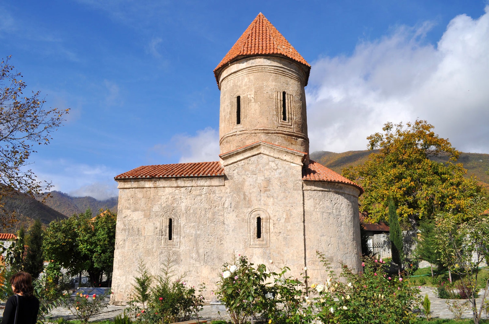 Kish Albanian stone church with a red roof in a scenic location with trees and mountains.