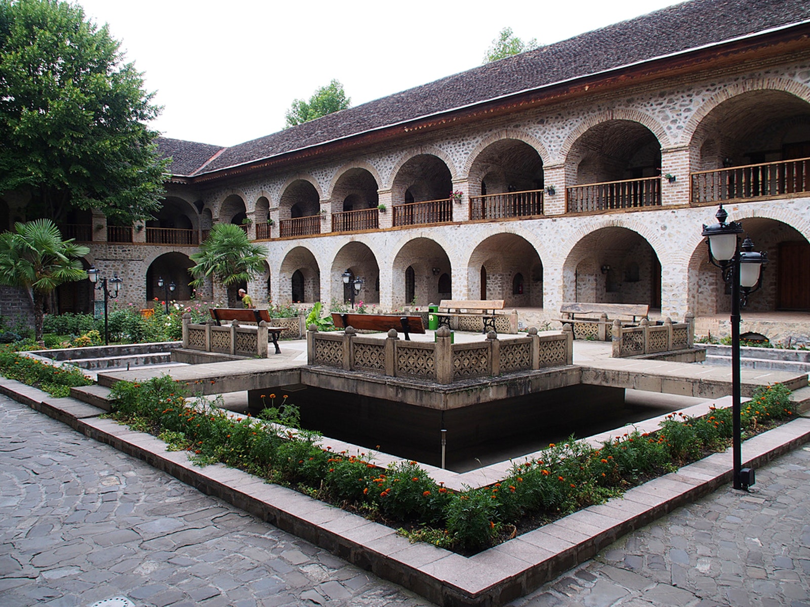 Sheki Caravanserai with arched windows and a courtyard with a fountain and garden.