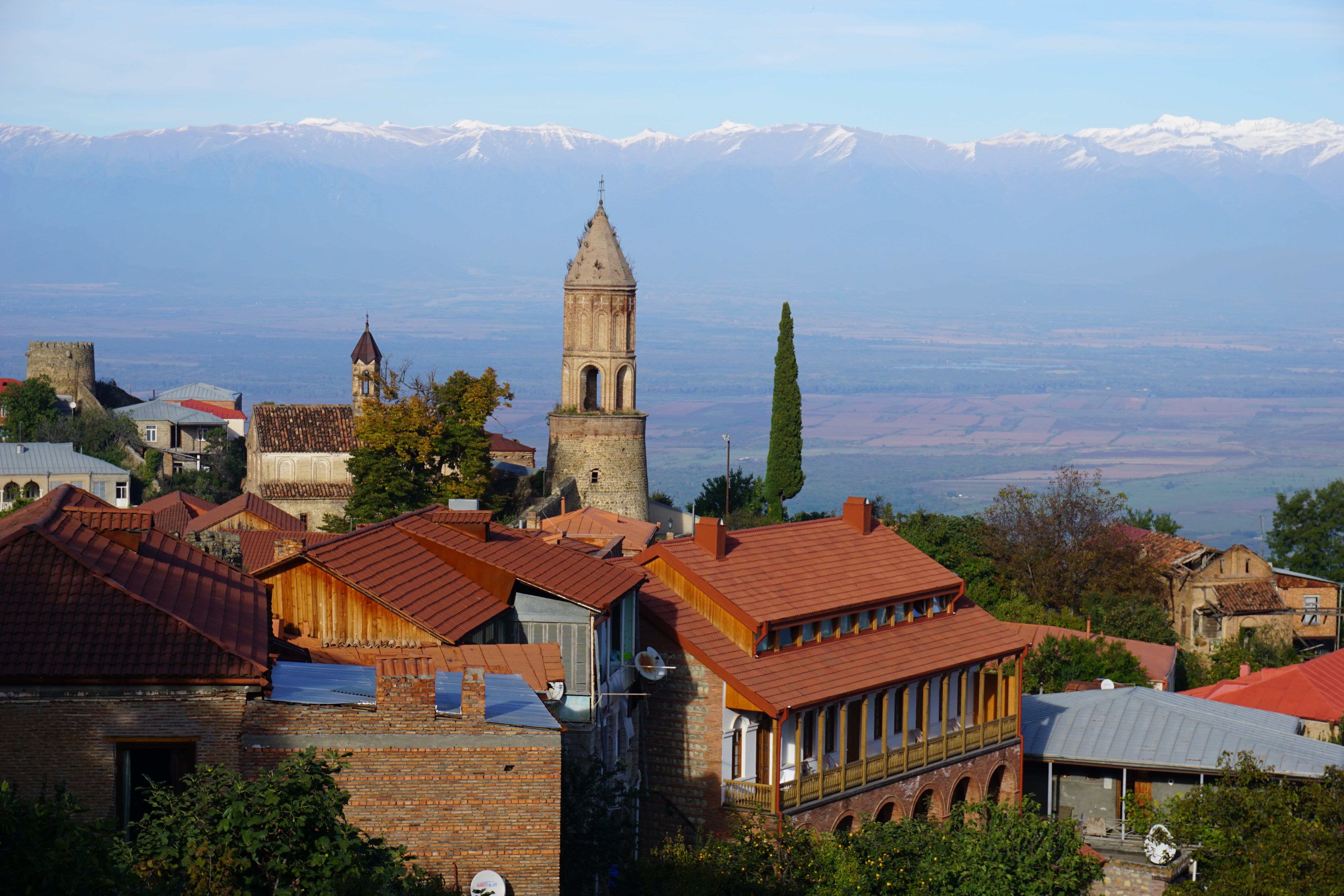 Sighnagi, Georgie with red-roofed buildings and a tall tower, set against a mountainous landscape.