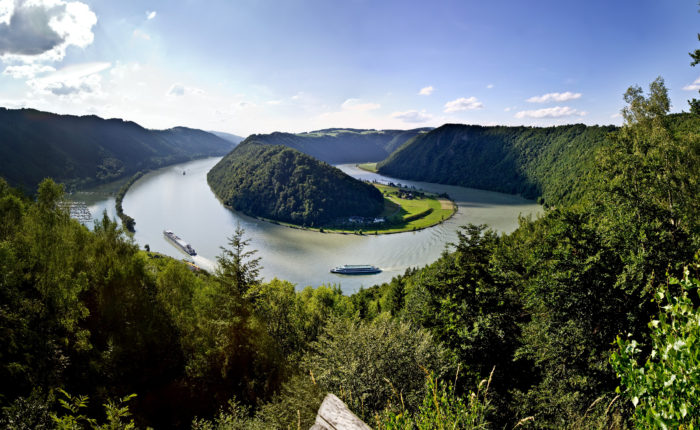 Cycling along the scenic Danube River with a boat in the background, part of the Danube Boat & Bike tour featuring picturesque landscapes, European countryside, and cultural landmarks.