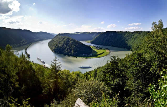 Cycling along the scenic Danube River with a boat in the background, part of the Danube Boat & Bike tour featuring picturesque landscapes, European countryside, and cultural landmarks.