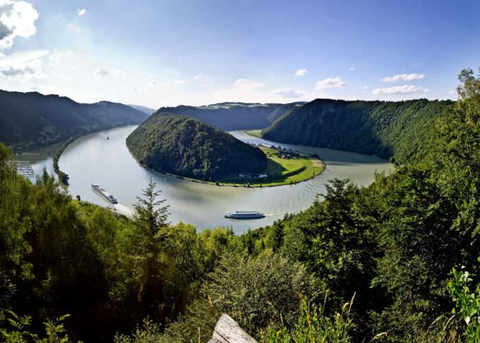 Cycling along the scenic Danube River with a boat in the background, part of the Danube Boat & Bike tour featuring picturesque landscapes, European countryside, and cultural landmarks.